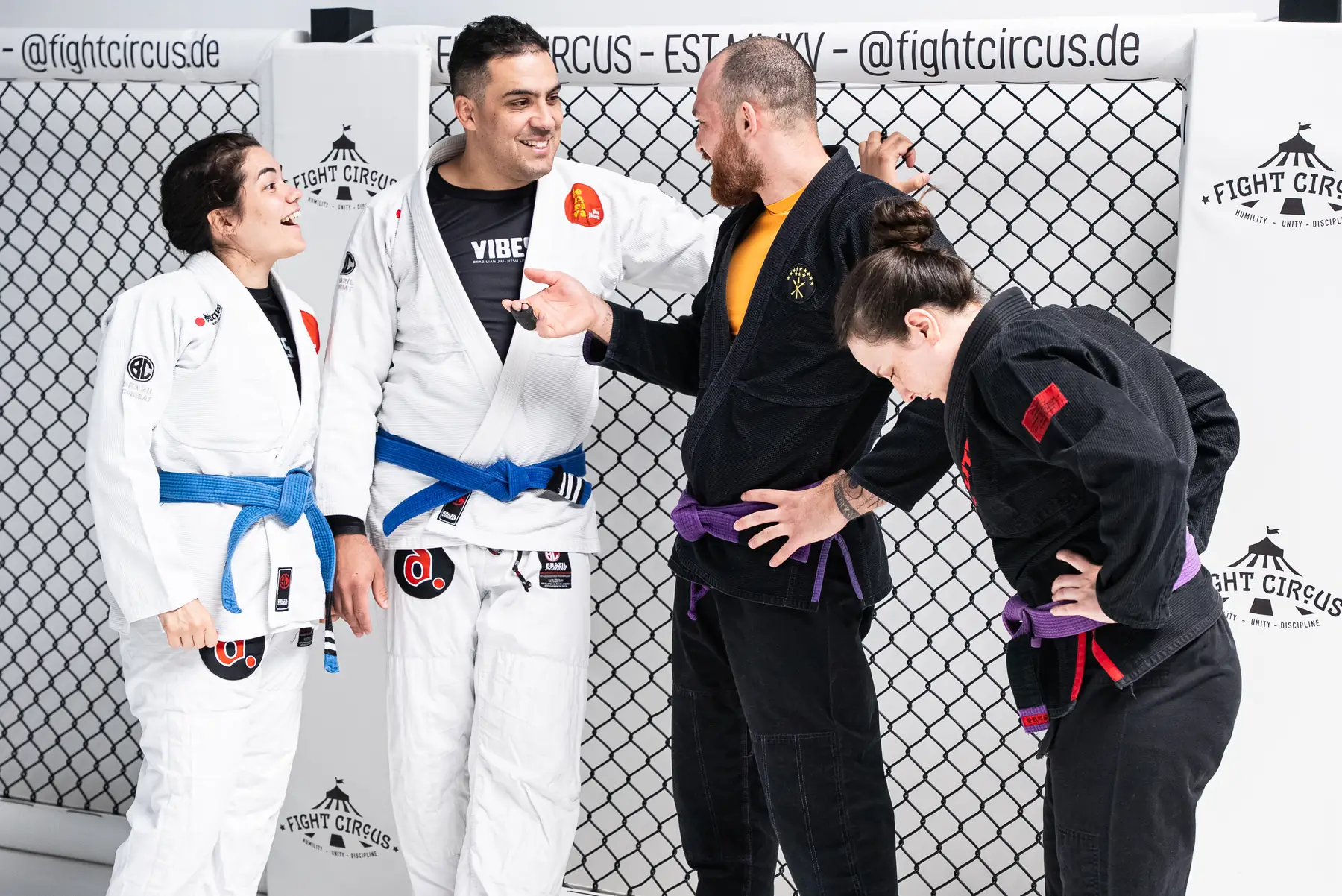Vier BJJ-Praktizierende im Gi lachen und unterhalten sich miteinander.